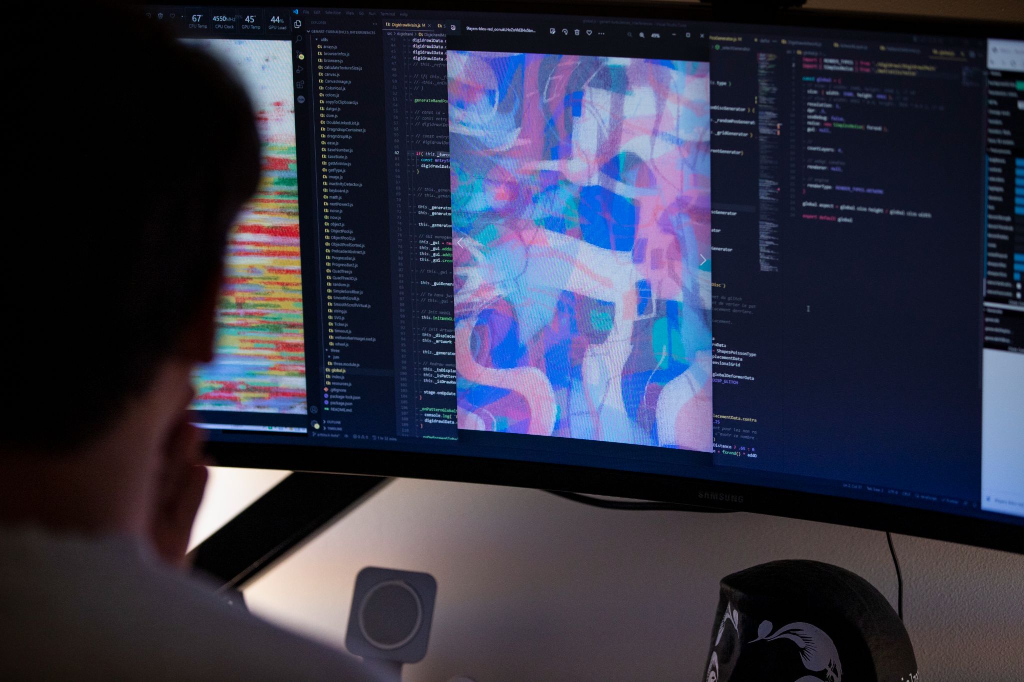 Artist working with code and generative artwork displayed on a wide monitor, code on left, vibrant abstract output in center